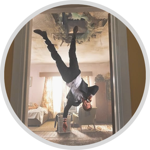 Image of Jack Quaid upside-down, with a huge hole in the ceiling. Hes wearing a business suit and talking on his cell phone in Novocaine (1)