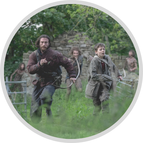 Image of a man and a boy sprinting across a deserted green village with zombies chasing after them