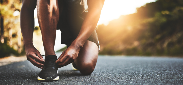 Image of a runner kneeling to tie their shoe on a mountainous road