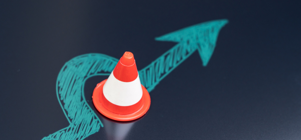 A teal arrow veers around an orange construction cone