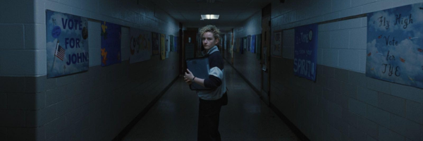 Julia Garner standing in a desolate, dark, school hallway clutching her binder in Weapons 