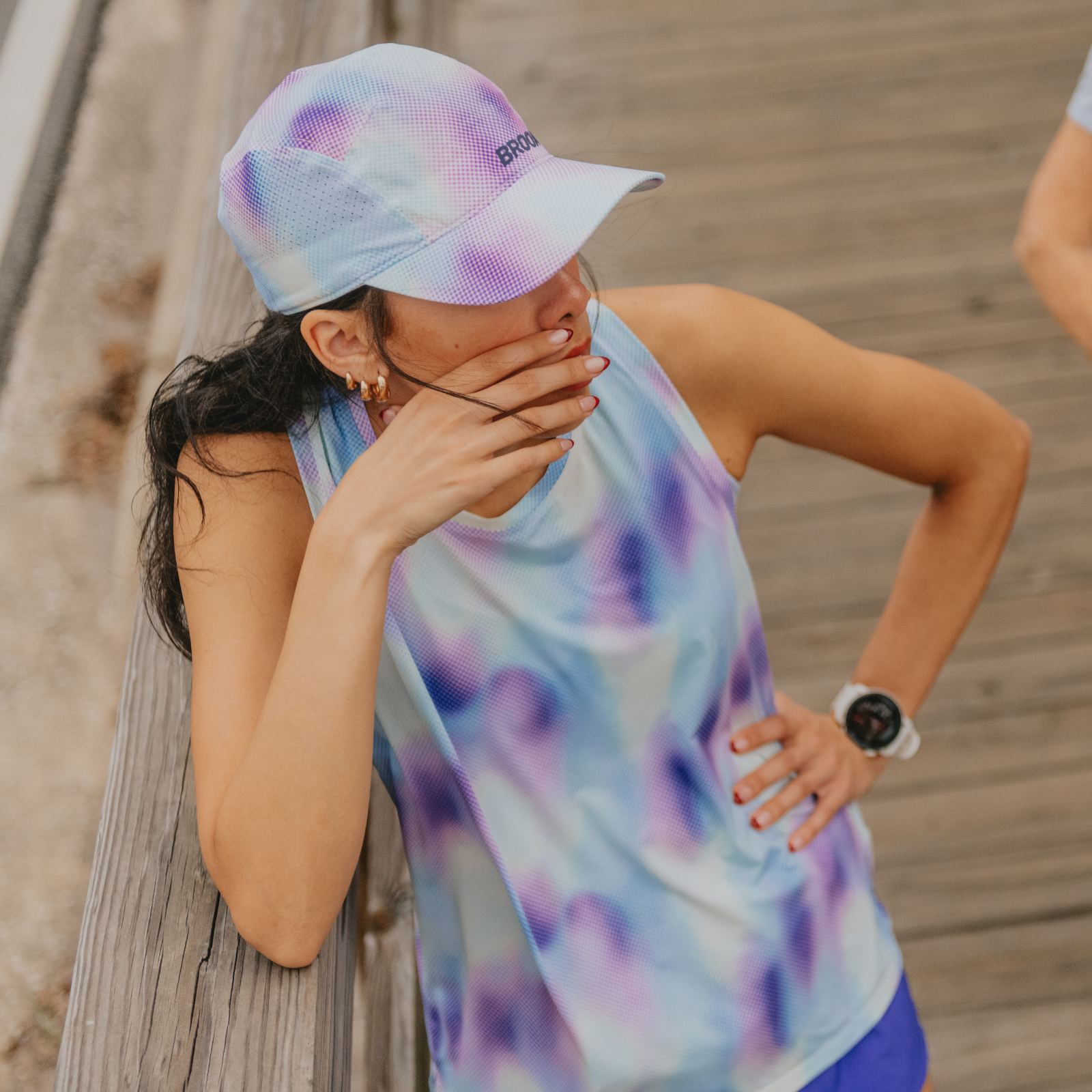 Woman standing on a bridge wearing a Brooks hat and tank