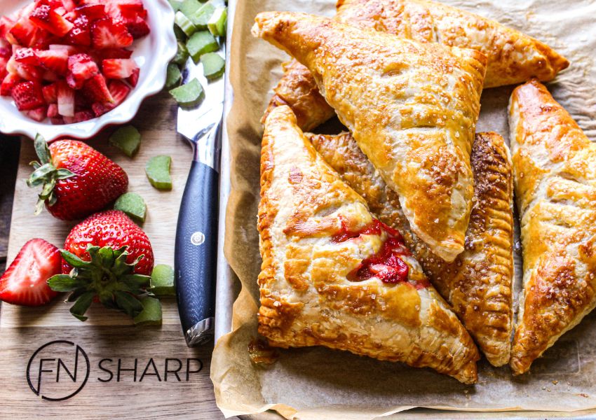 F.N. Sharp Utility Knife with strawberries and rhubarb on cutting board with baked strawberry-rhubarb hand pies