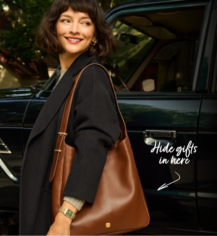 Woman in a black blazer looks back stylishly, carrying the brown leather Dillon Hobo with “Hide Gift in Here” callout.