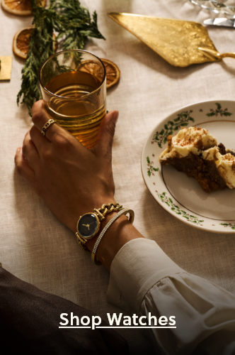 Woman’s arm in white blouse rests on a holiday table, holding a drink beside dessert, with a gold watch and bracelet stack visible and cta to shop watches