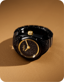 A close-up of a black metal watch ring with a circular case and a black dial with gold details