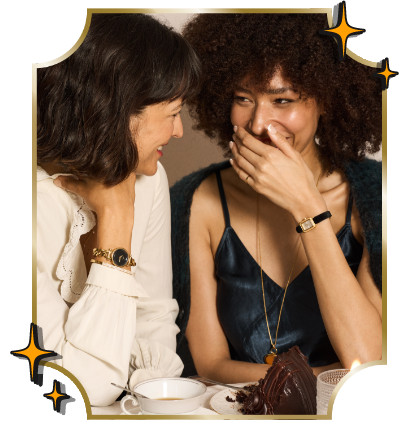 Two women laugh at a holiday-decorated table with tea, cake, and wearing elegant Fossil dress watches