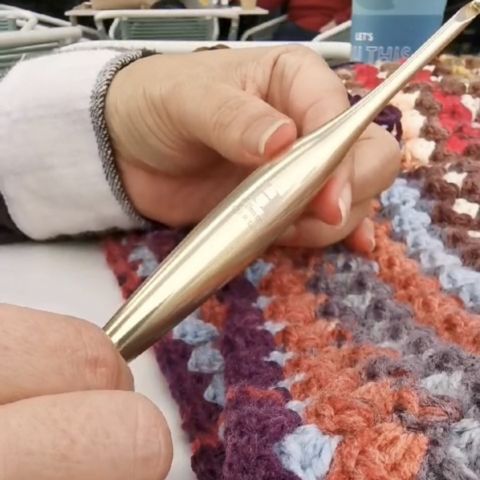 Hand holding a gold Furls crochet hook in front of a colorful crochet project