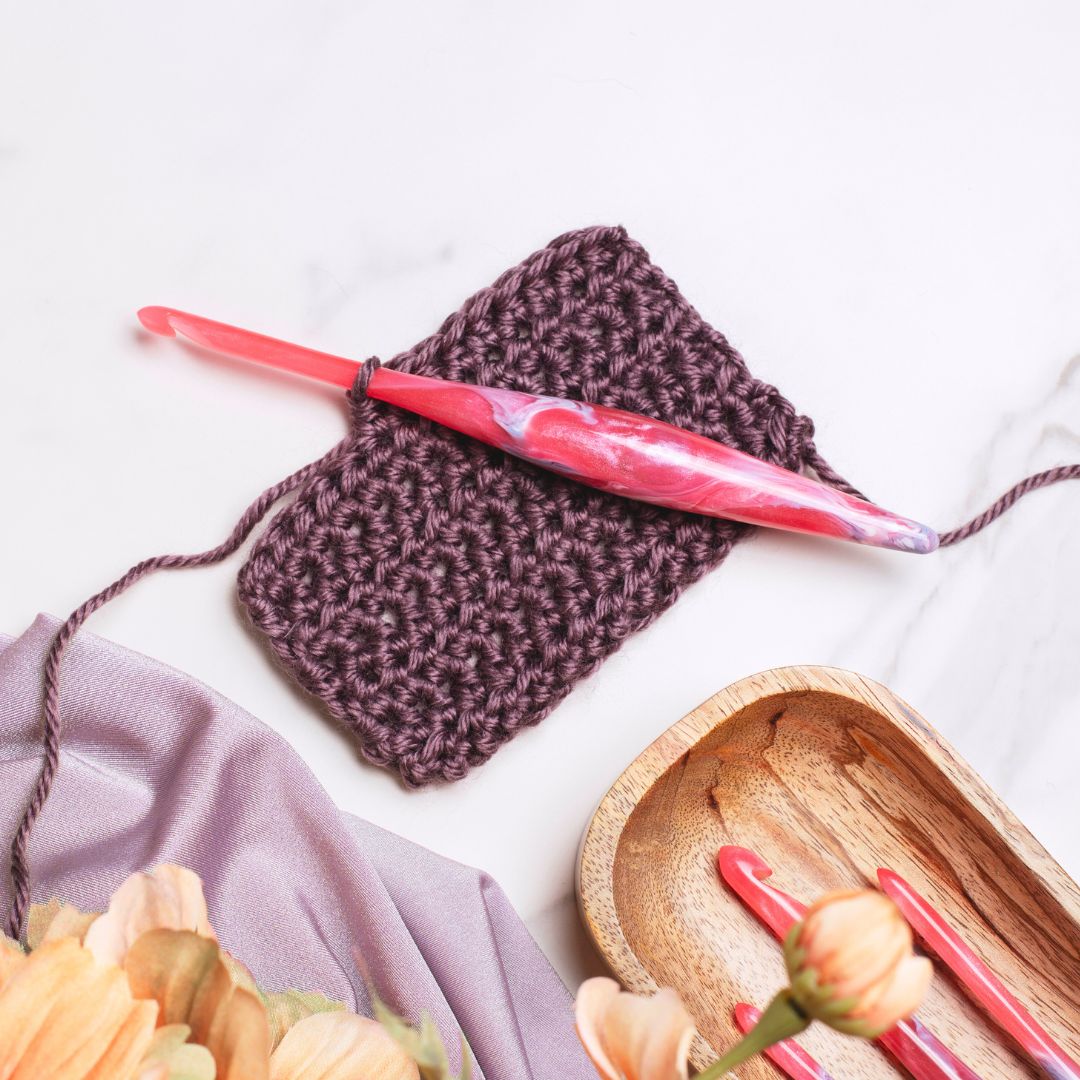 A pink resin crochet hooks with swirls of lavender, on a crochet swatch