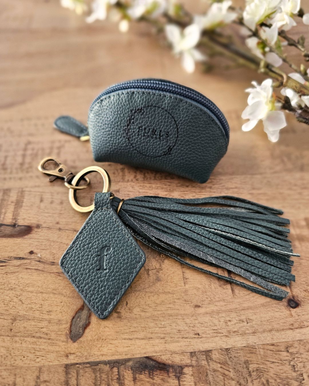 A set of dark green leather accessories: a zip pouch and a tassel keychain