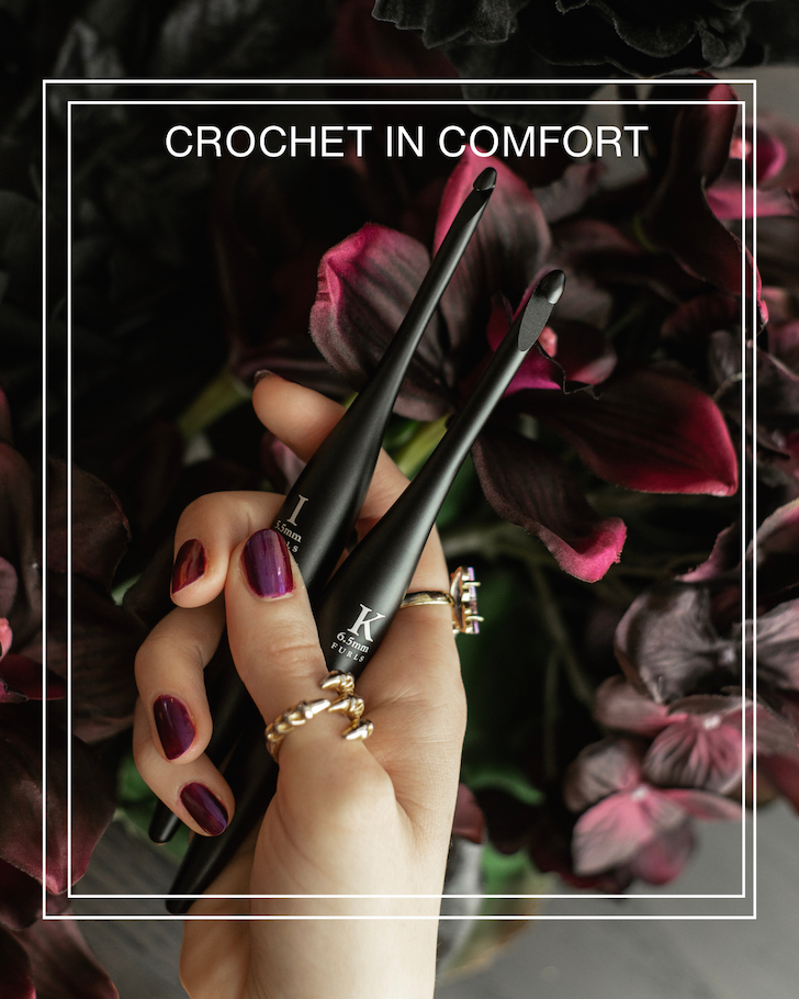 crochet in comfort.  A hand holds two streamline metal onyx crochet hooks above deep red and black flowers.