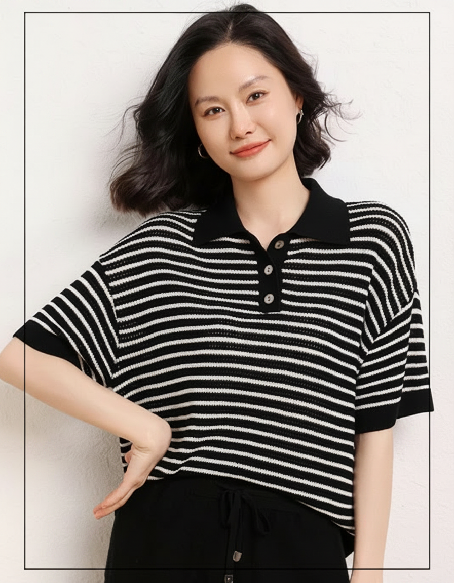 A woman in a black and white striped polo shirt smiles, with her hand on her hip.
