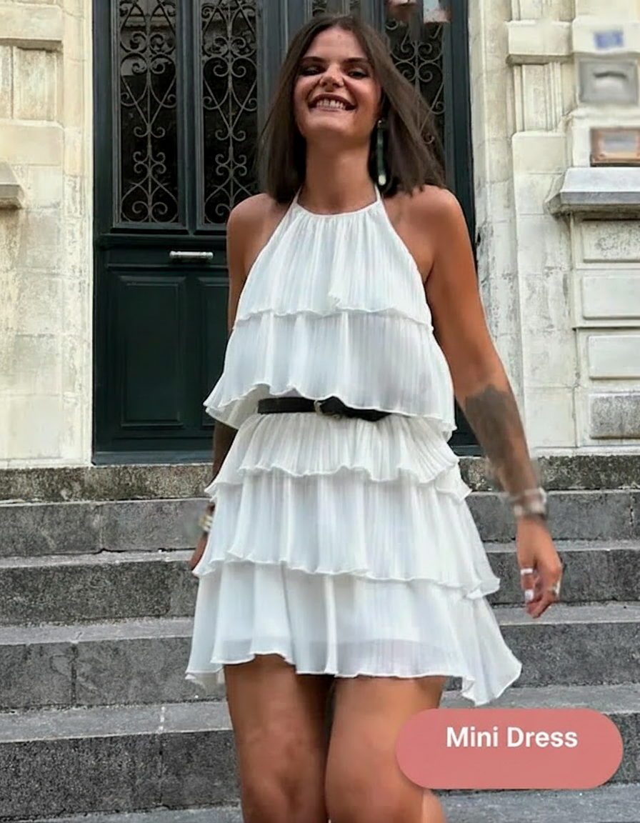 Woman in a white tiered mini dress smiles on stone steps.