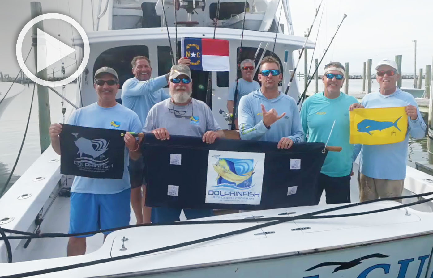 Members of the Dolphinfish Research Program holding flags with their logo in the cockpit of a boat