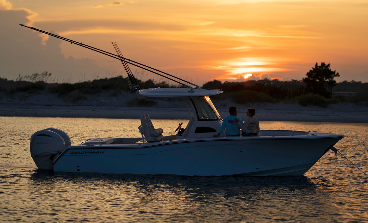 A couple sitting in the bow of a Grady-White boat watching the sun set.