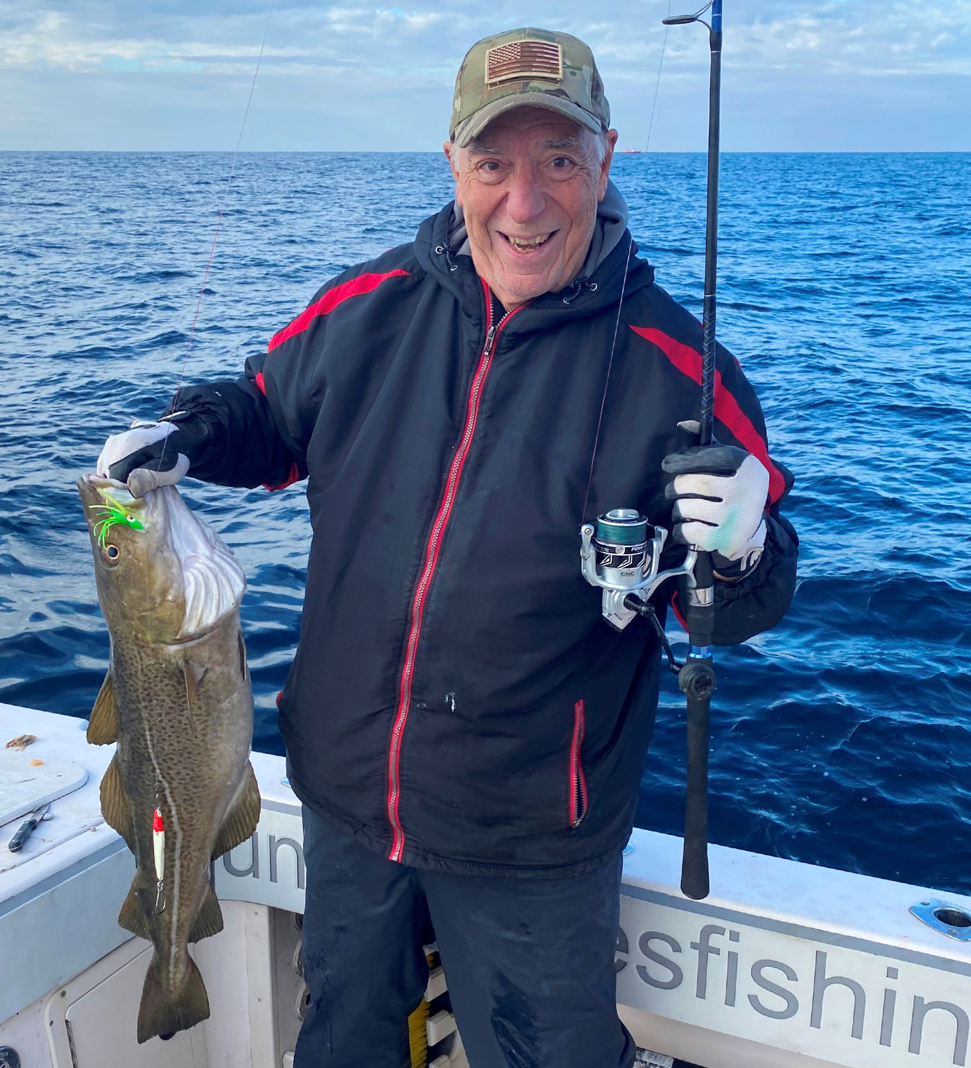 Captain John Raguso in the cockpit of a Grady-White boat holding a fishing rod and caught fish.