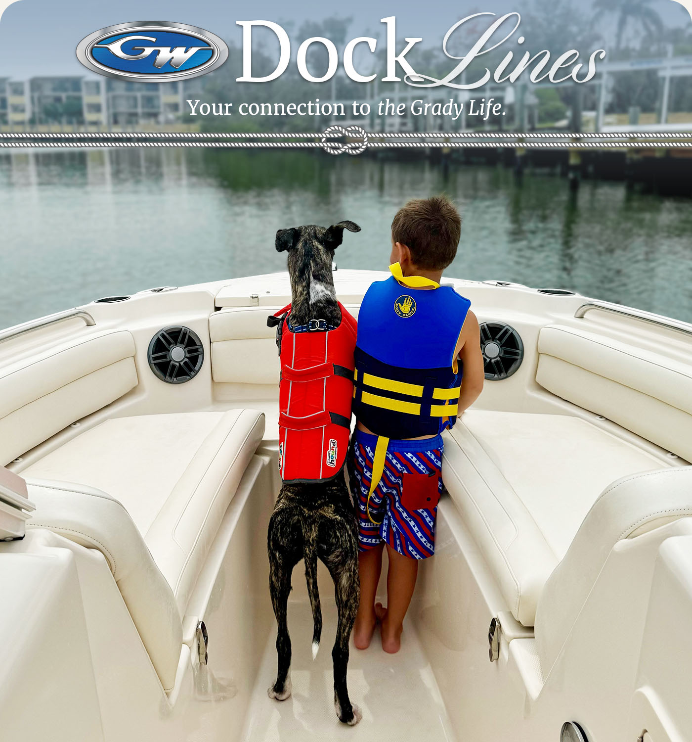 A boy and his dog wearing PFDs while looking out from the bow of a Grady-White boat on a calm waterway.