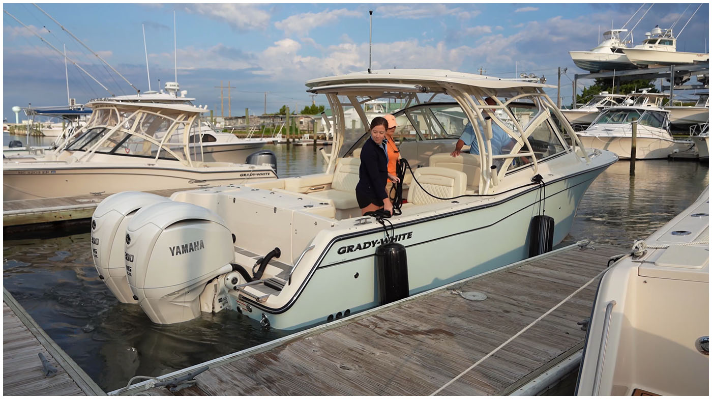 Two people holding dock lines in the cockpit of a Grady-White Freedom 307 dual console boat while preparing to tie it up in a marina slip.