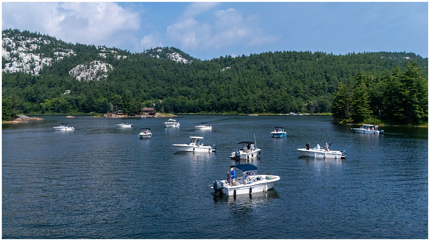 An aerial shot of several Grady-White boats gathering on the water near a rocky, tree-lined shoreline.