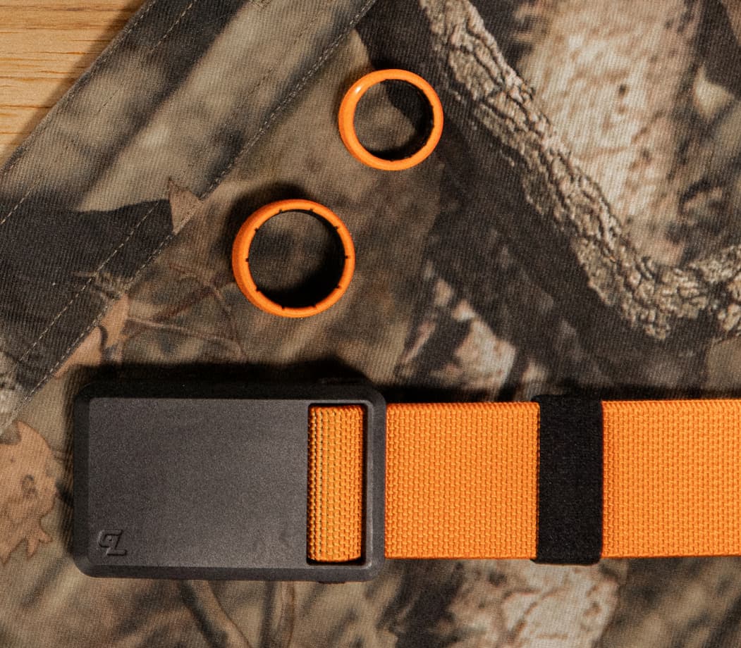 Photo of new Blaze orange Zeus rings and Ultra belt on top of a camo background.
