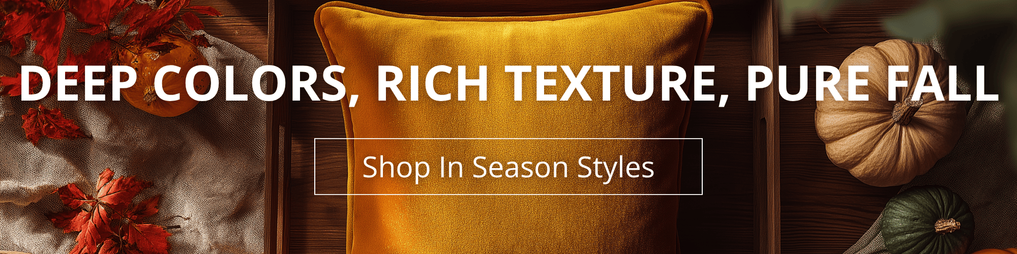 Promotional banner with a cozy autumn theme. A golden velvet pillow is centered on a wooden surface, surrounded by pumpkins and red fall leaves. Large white text reads ‘Deep Colors, Rich Texture, Pure Fall.’ Below, a boxed button says ‘Shop In Season Styles.