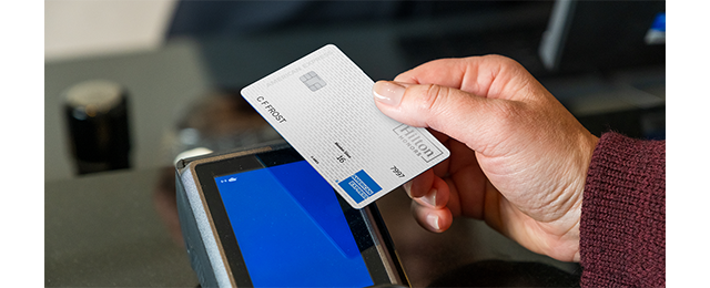 Hand holding Amex card near payment terminal.