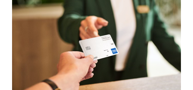 Person handing a Hilton Honors Amex card to a hotel staff member in a green blazer.