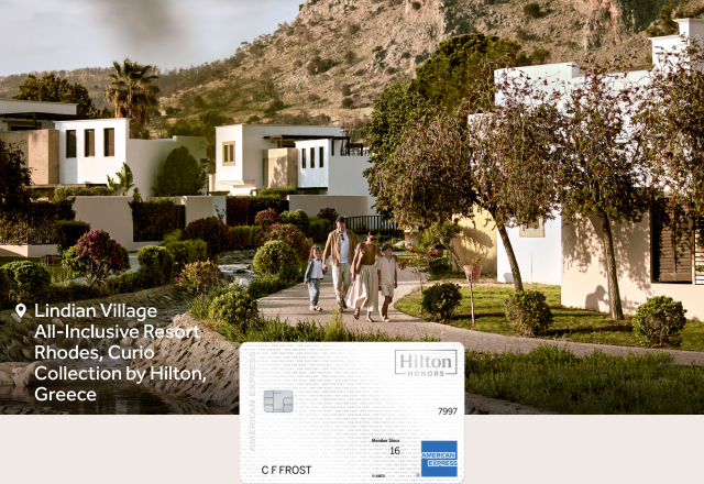 A family walks through gardens at Lindian Village All-Inclusive Resort Rhodes, Curio Collection by Hilton, Greece with a Hilton Honors Amex card visible.
