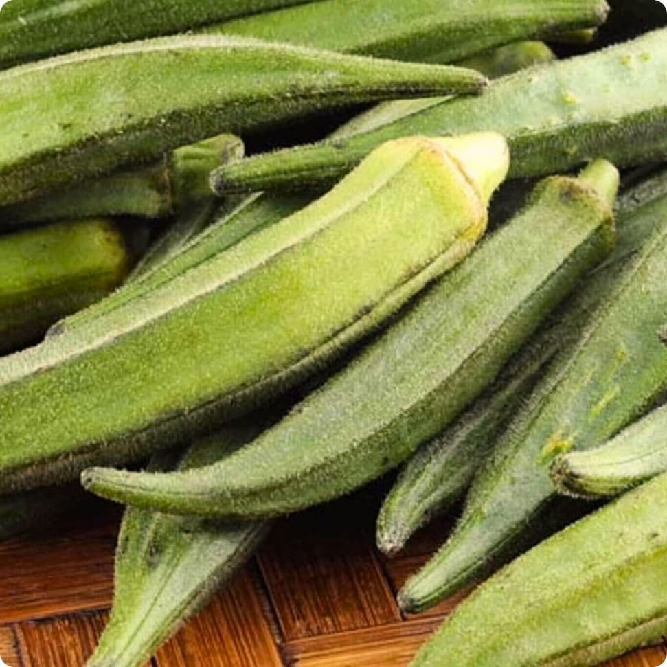 Fresh green okra pods piled together on a wooden surface.