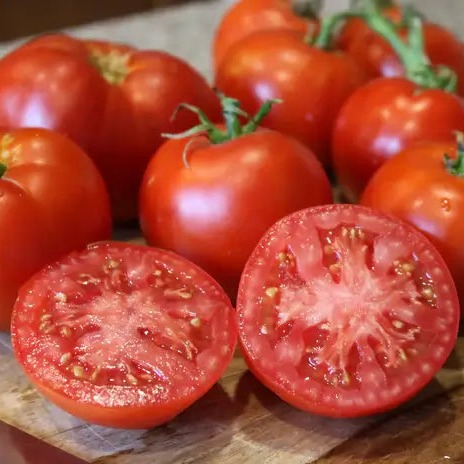 Whole and sliced Better Boy Plus tomatoes on a cutting board.