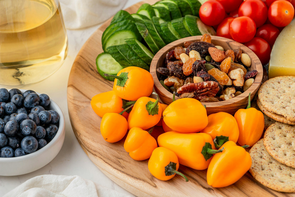 an image of a plate of fruit and vegetables with crackers and a glass of wine