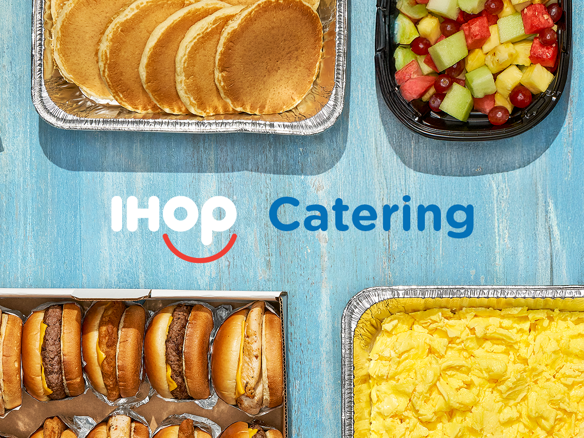 Catering items in serving trays, including pancakes, fruit mix, burgers and chicken sandwiches, and scrambled eggs.