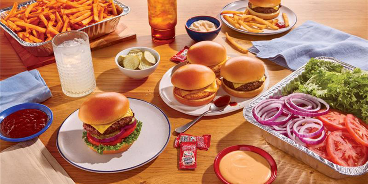 An IHOP Catering spread is on a table, including burgers, chicken sandwiches, and a tray of fixins.
