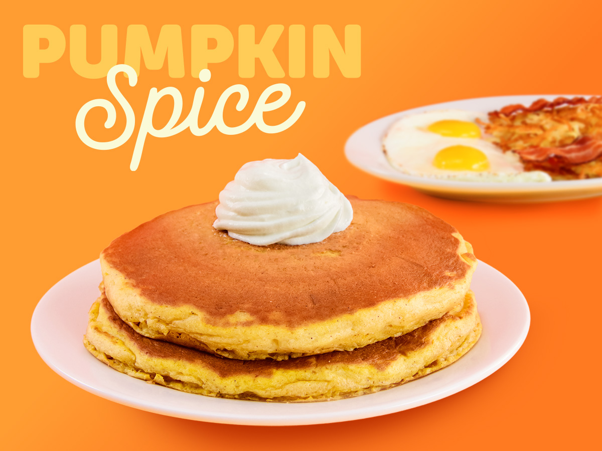 Two Pumpkin Spice Pancakes with whipped topping, and a side of eggs, bacon and hash browns in the background.