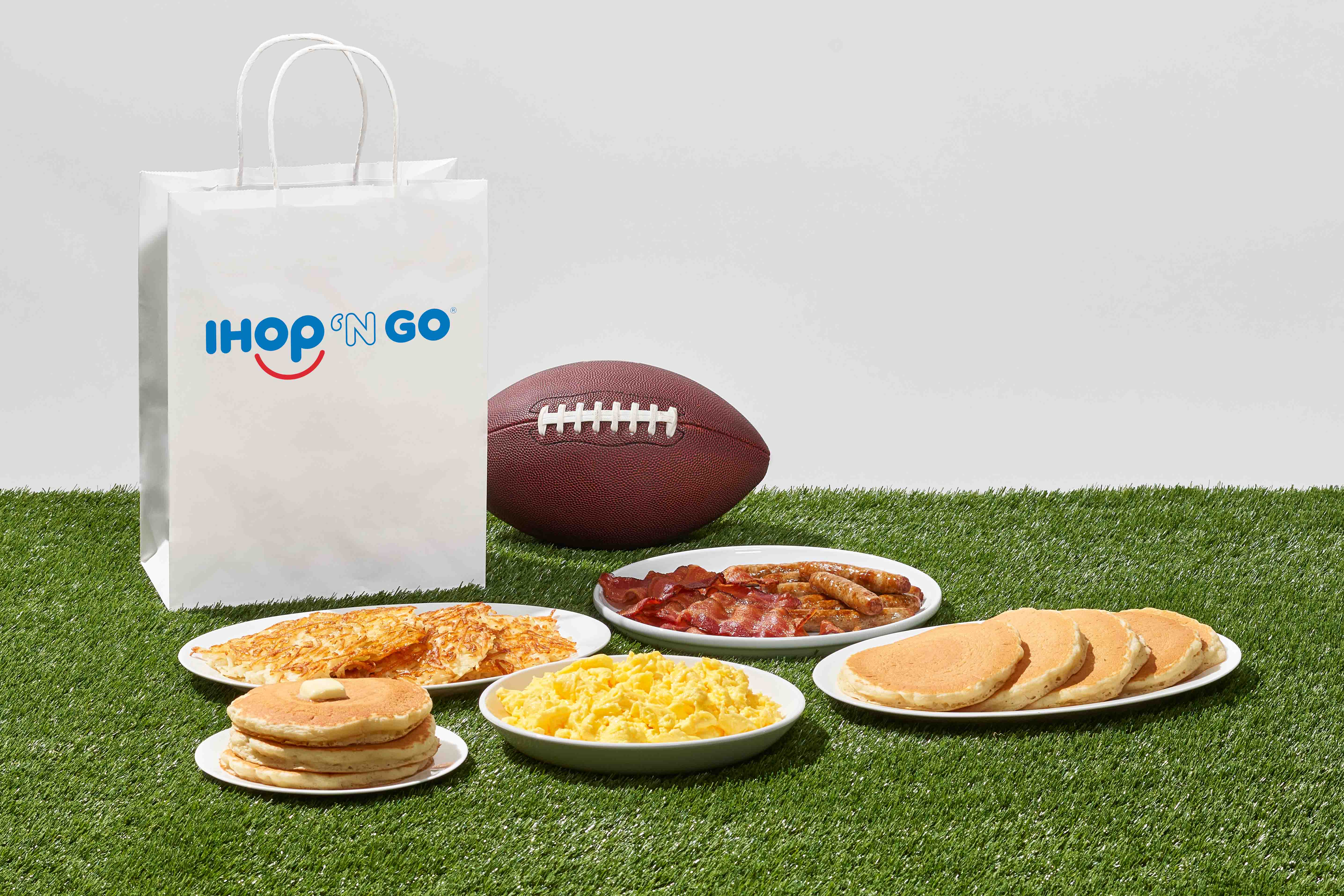 Plates of IHOP food are on turf, along with a football and to go bag.