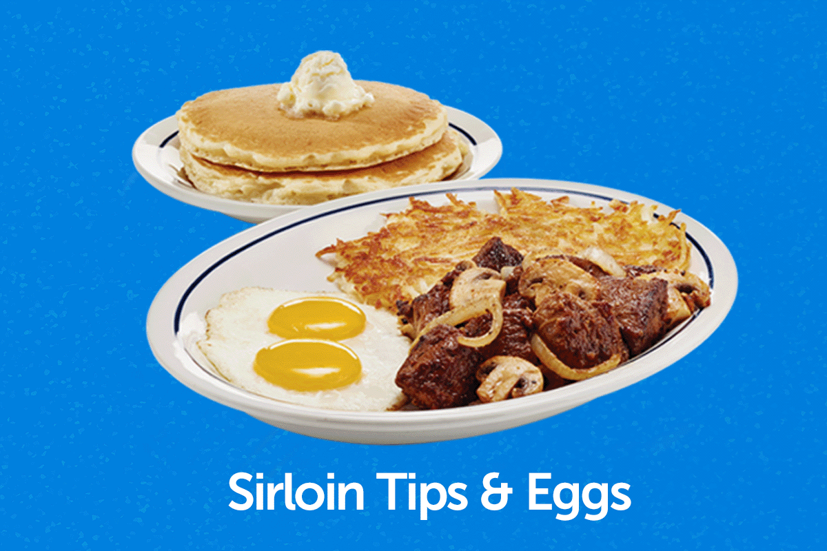  The Sirloin Tips & Eggs meal, with sirloin tips topped with mushrooms, two sunny side up eggs, and hash browns on a plate. Another plate of two buttermilk pancakes topped with butter is behind it.
