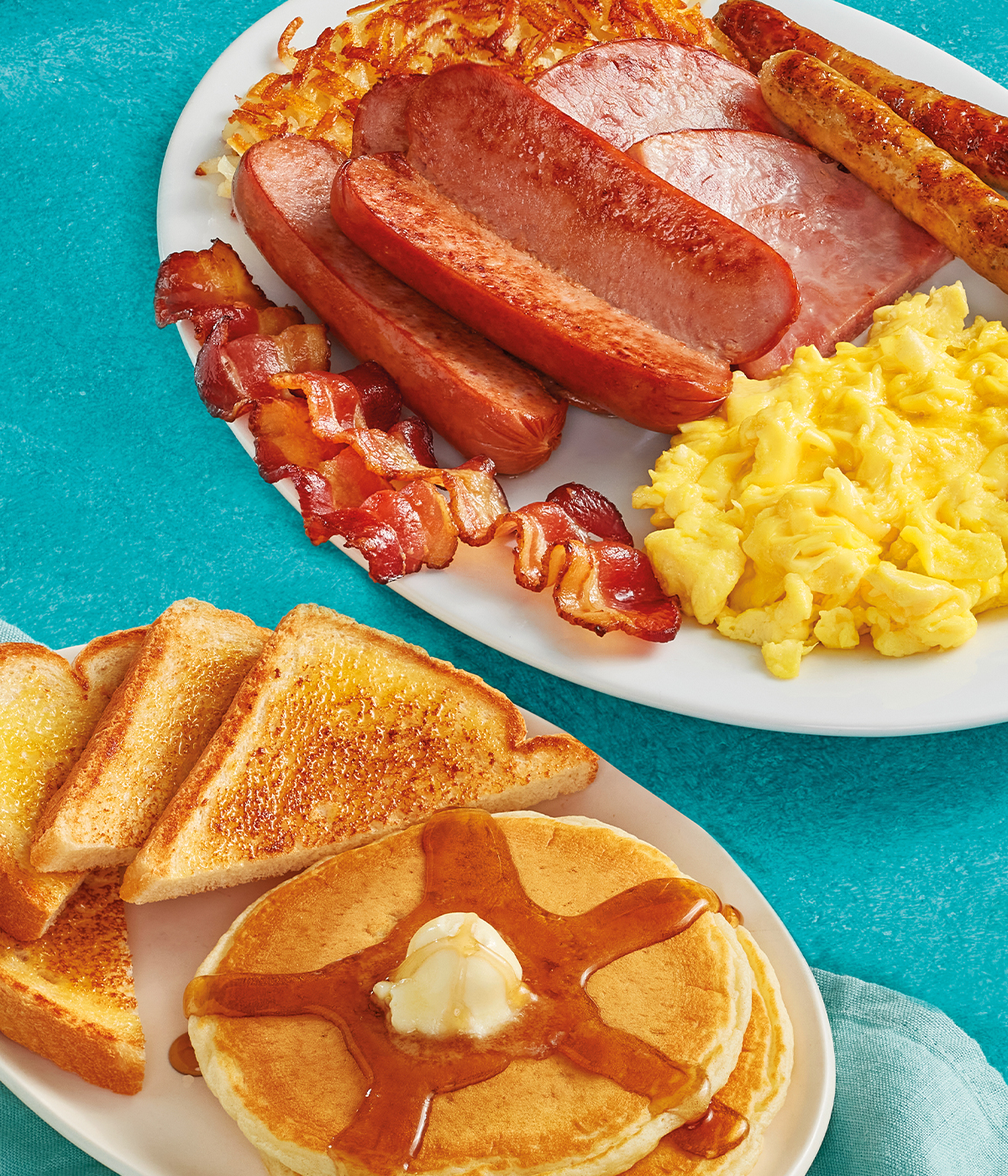 Two eggs served your way, two pork sausage links, two slices of thick-cut ham, two strips of hickory-smoked bacon, and hash browns on a plate. Served with 2 buttermilk pancakes topped with syrup and butter and a slice of toast.