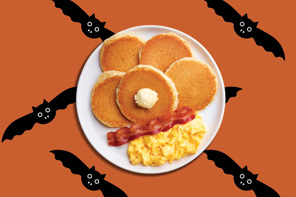 The Silver 5 pancakes, along with scrambled eggs and a bacon strip, are against an orange background with cartoon bats.