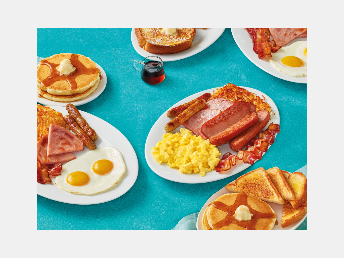 IHOPs BreakFEASTs set on a blue tabletop. Features plates of hashbrowns, eggs, bacon, sausage, pancakes, and toast.