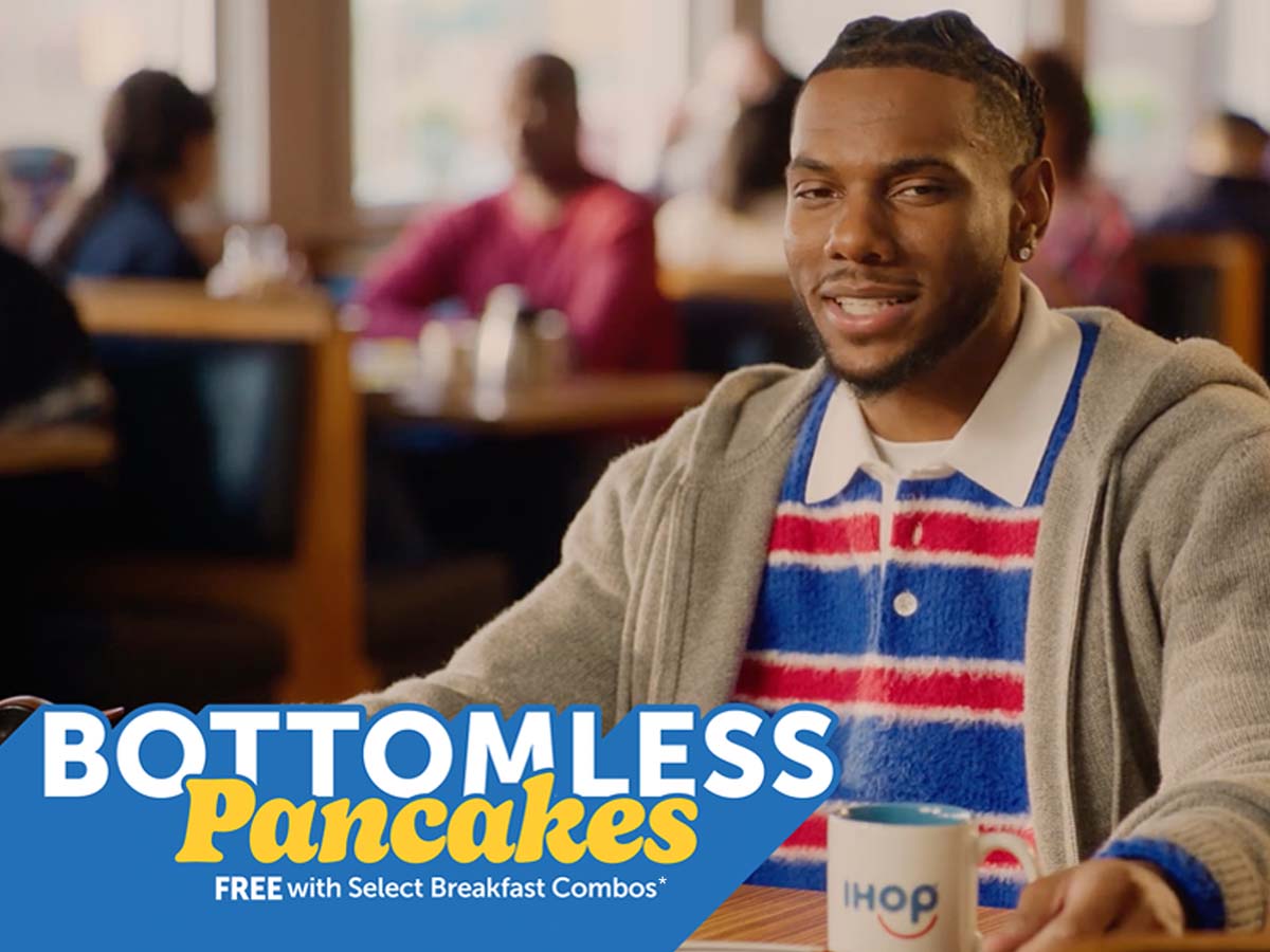 Malik Nabers seated at an IHOP booth, wearing a collared red and blue striped shirt with a grey sweatshirt over it.