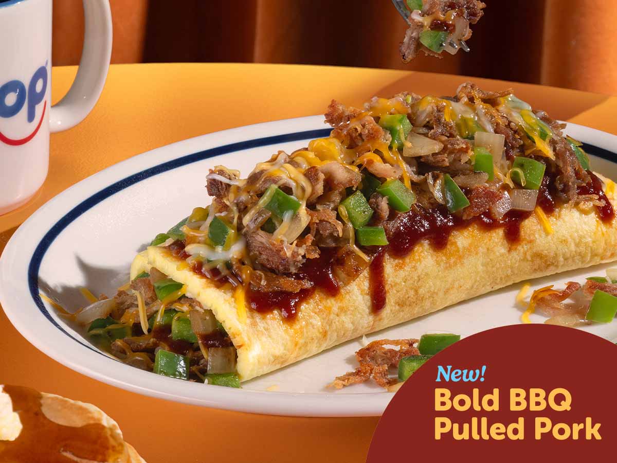 The Bold BBQ Pulled Pork Omelette on a plate on a table in an IHOP booth, with an IHOP mug beside it