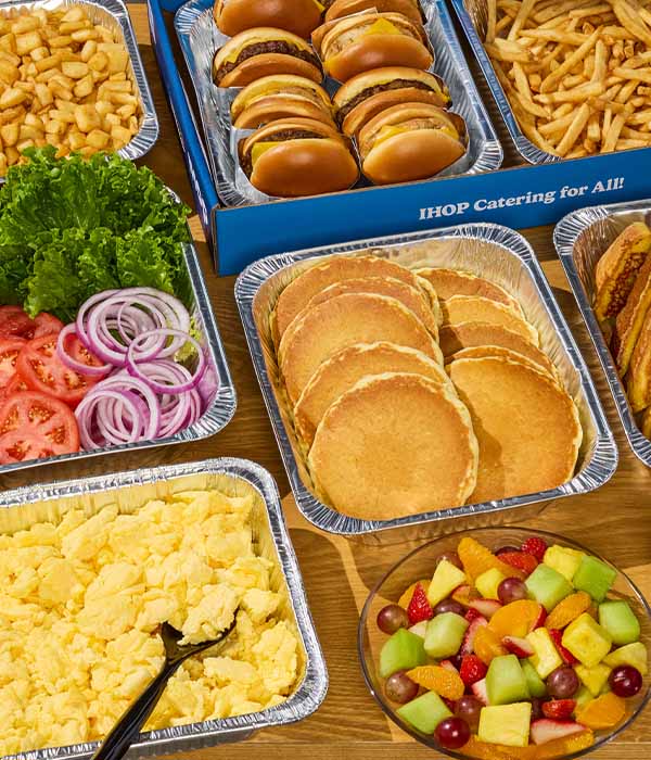 A full IHOP Catering spread, with tins of pancakes, french toast, scrambled eggs, and more.