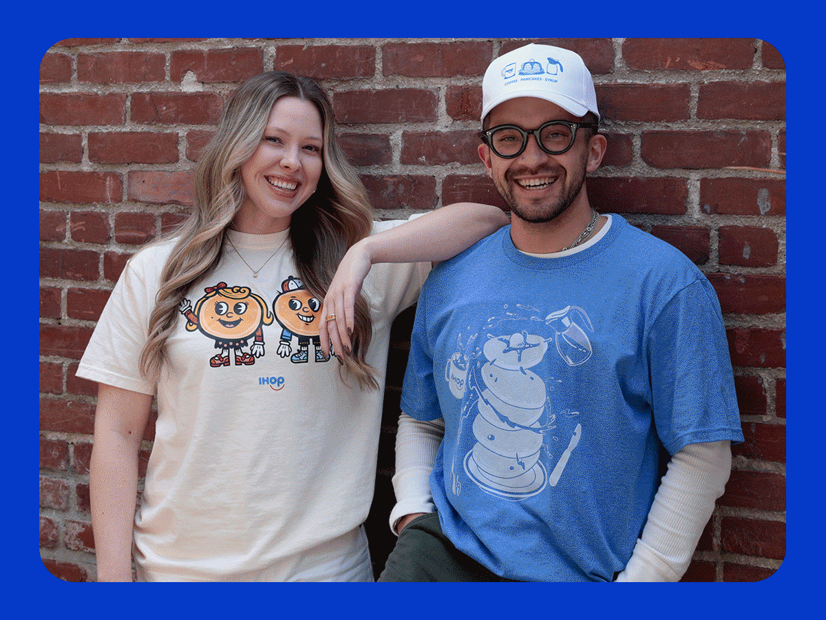 A woman and man wearing IHOP t-shirts smile and stand against a brick wall