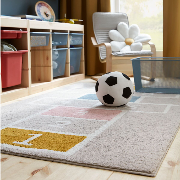 A STÄPPSPARV rug featuring a hopscotch pattern placed in a children’s room with a textile soccer ball and mesh storage units. 