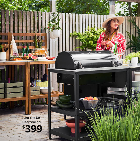 A woman stands on her patio with the GRILLSKÄR charcoal grill.