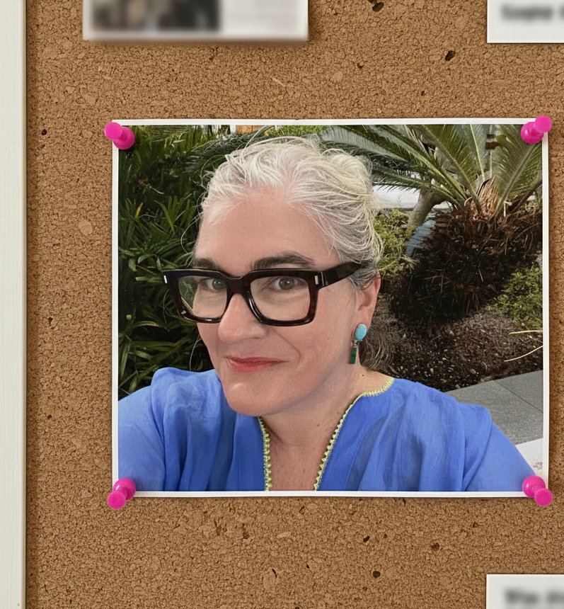 Woman with gray hair and glasses smiles at the camera, pinned to a corkboard.