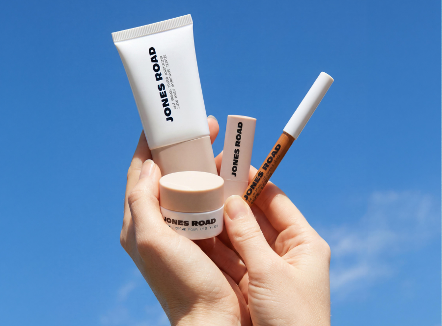 Hands holding four Jones Road Beauty products against a bright blue sky