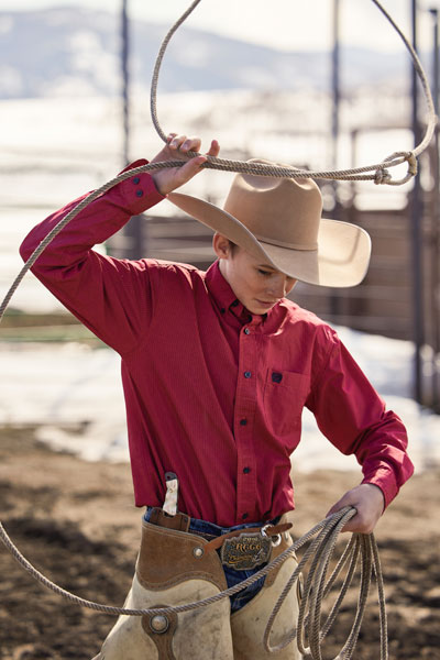 A boy wearing a cowboy hat while swinging a lasso. 