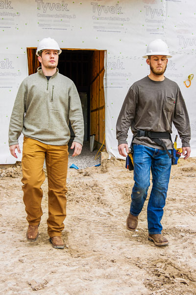 To men wearing Justin work boots while walking on a job site.