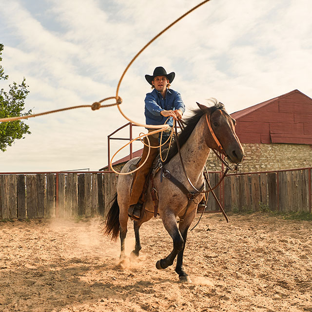 A cowboy on a horse twirling a lasso.